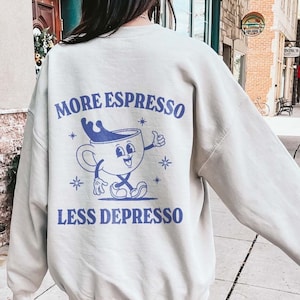 Puede incluir: Una sudadera beige con un gr&aacute;fico de una taza de caf&eacute; y el texto "More Espresso Less Depresso" impreso en la espalda.