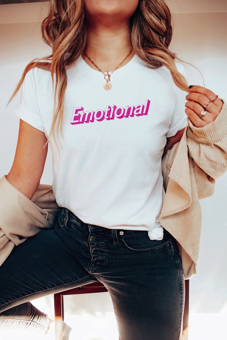 May include: A white t-shirt with the word "Emotional" printed in pink 3D lettering.