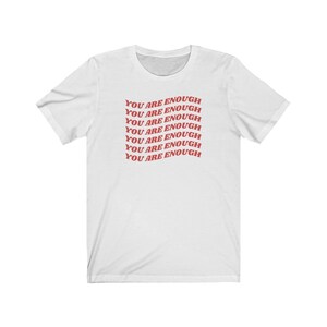 May include: White t-shirt with the phrase "You are enough" repeated in red text.
