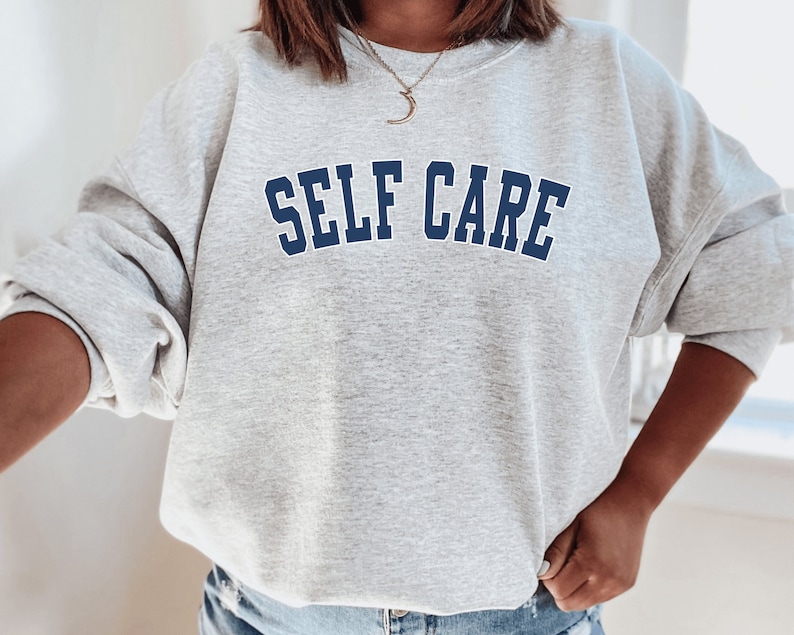 Peut inclure: Sweat-shirt gris avec le texte "SELF CARE" en lettres bleues soulign&eacute;es.