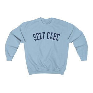Peut inclure: Un sweat-shirt bleu clair avec le texte "SELF CARE" en bleu marine.