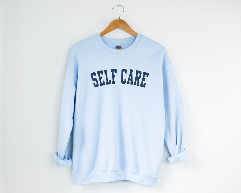 Peut inclure: Un sweat-shirt bleu clair avec le texte "SELF CARE" imprim&eacute; en bleu marine.