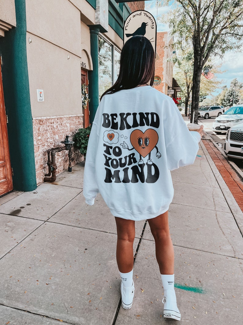 K&ouml;nnte beinhalten: Wei&szlig;er Pullover mit einem grafischen Aufdruck eines Comic-Herzens mit Augen und einer Gedankenblase, auf der "Be Kind To Your Mind" steht.