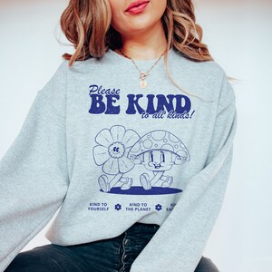 May include: Gray sweatshirt with a blue graphic of a mushroom character and the text "Please Be Kind to all kinds!" with three smaller icons below that say "Kind to Yourself", "Kind to the Planet", and "Kind to Each Other".