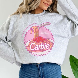 Może przedstawiać: Szara bluza z nadrukiem w kolorze r&oacute;żowym i ż&oacute;łtym przedstawiającym talerz spaghetti z tekstem "Come On Carbie Let's Go Party" i "This Carbie Regrets Nothing" oraz słowem "Carbie" w dużym rozmiarze czcionki.