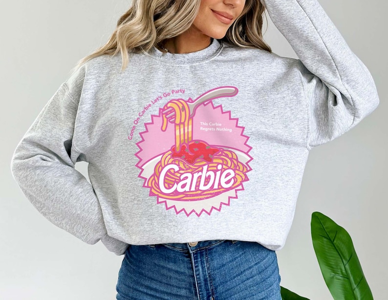Może przedstawiać: Szara bluza z nadrukiem w kolorze r&oacute;żowym i ż&oacute;łtym przedstawiającym talerz spaghetti z tekstem "Come On Carbie Let's Go Party" i "This Carbie Regrets Nothing" oraz słowem "Carbie" w dużym rozmiarze czcionki.