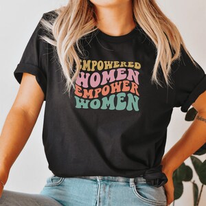 May include: A black t-shirt with a retro-style graphic that says "Empowered Women Empower Women" in rainbow colors.