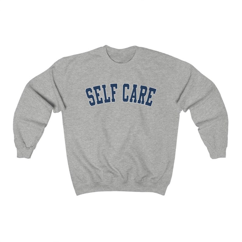 Peut inclure: Un sweat-shirt gris avec le texte "SELF CARE" en lettres bleues marine.