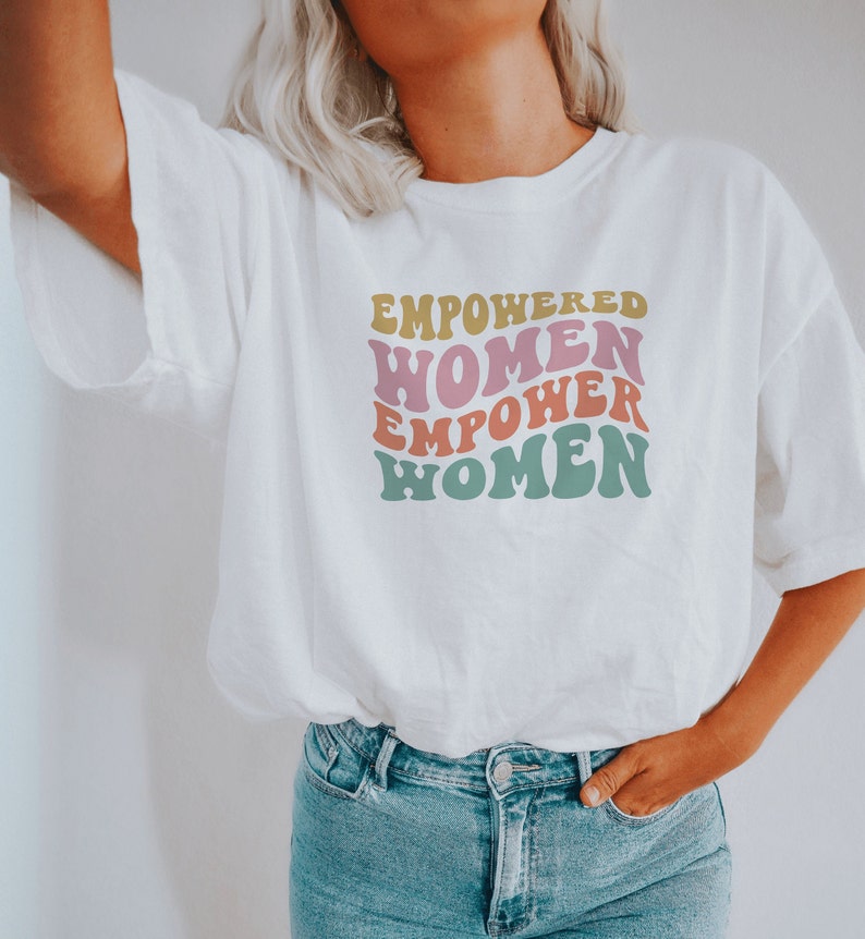 May include: White t-shirt with a graphic print that says "Empowered Women Empower Women" in a retro font with pink, yellow, and green colors.
