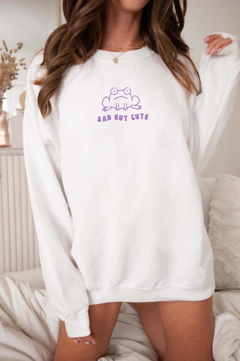 May include: White sweatshirt with a purple frog graphic and the text "sad but cute".