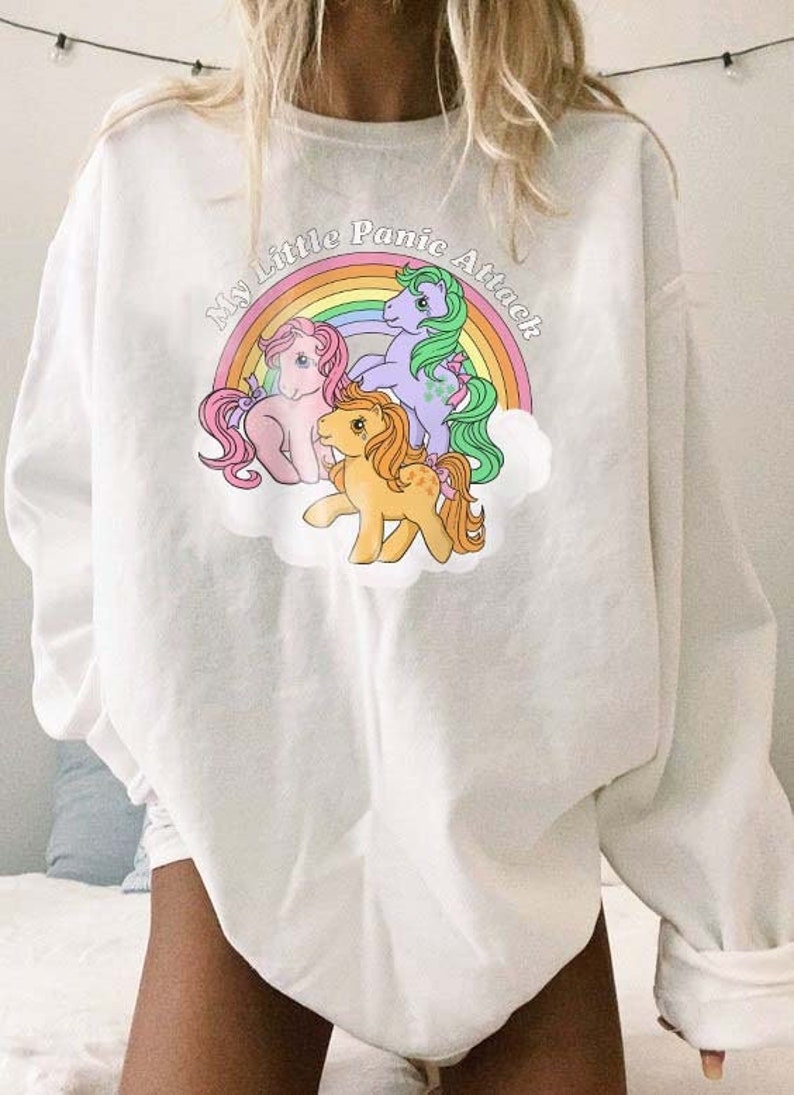 May include: White long-sleeve sweatshirt with a rainbow and three My Little Pony figures. The text "My Little Panic Attack" is printed on the sweatshirt.