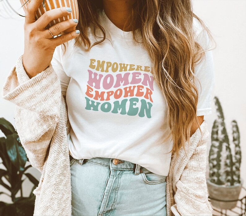 May include: White t-shirt with a retro-style graphic that says "EMPOWERED WOMEN EMPOWER WOMEN" in pink, orange, and blue.