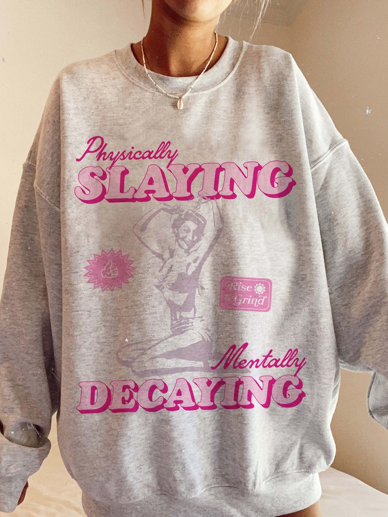May include: Gray sweatshirt with a pink graphic print that says "Physically Slayin'" and "Mentally Decaying". The graphic also includes a silhouette of a woman in a dance pose and a small graphic that says "Rise & Grind".