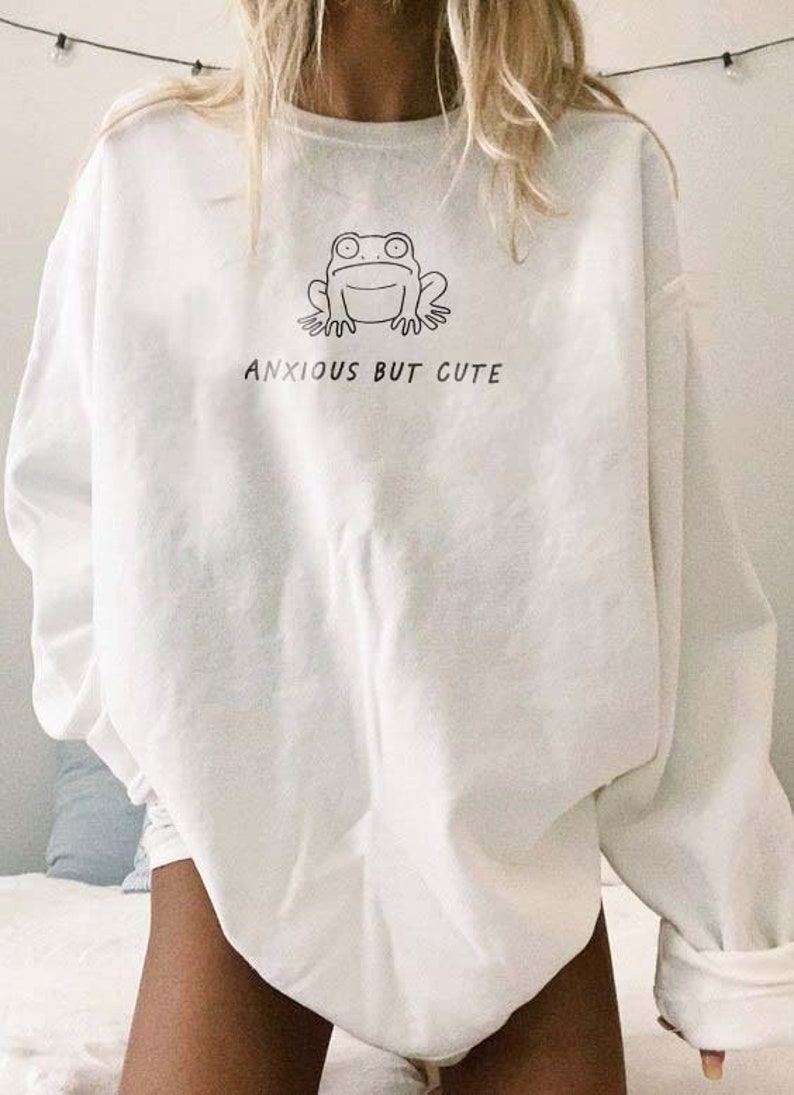 May include: White long-sleeved sweatshirt with a black line drawing of a frog and the text "ANXIOUS BUT CUTE".