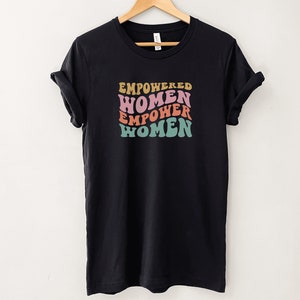 May include: Black t-shirt with a graphic print of the text "EMPOWERED WOMEN EMPOWER WOMEN" in a retro font with pink, orange, and teal colors.