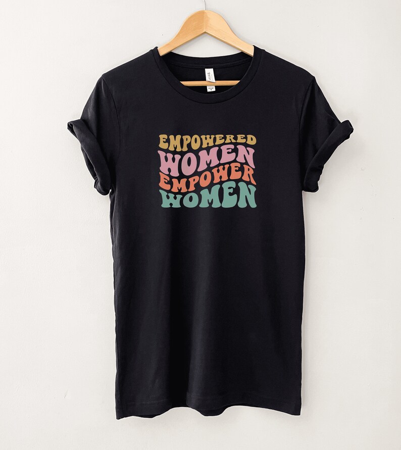 May include: Black t-shirt with a graphic print of the text "EMPOWERED WOMEN EMPOWER WOMEN" in a retro font with pink, orange, and teal colors.