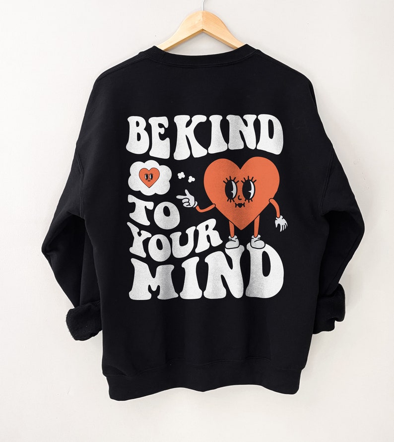 K&ouml;nnte beinhalten: Schwarzer Sweatshirt mit einem wei&szlig;en Grafikdruck, auf dem "Be Kind to Your Mind" steht. Die Grafik zeigt ein Cartoon-Herz mit Augen und einem Mund, das einen Finger zur Seite h&auml;lt.