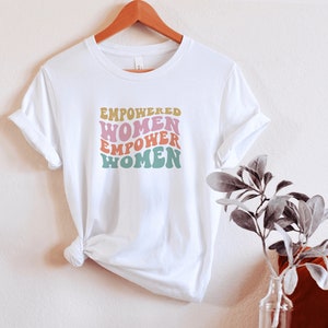May include: White t-shirt with the text "EMPOWERED WOMEN EMPOWER WOMEN" in a retro font with pink, yellow, green, and blue colors.