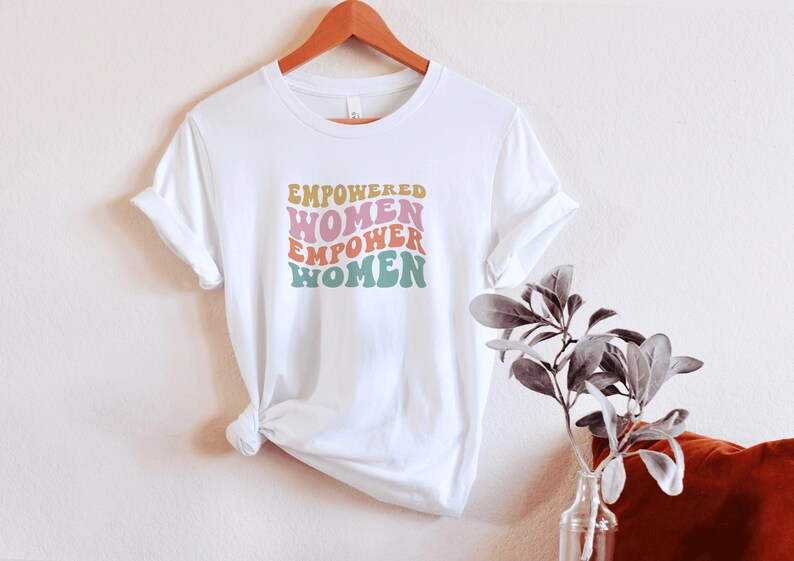 May include: White t-shirt with the text "EMPOWERED WOMEN EMPOWER WOMEN" in a retro font with pink, yellow, green, and blue colors.