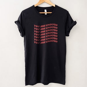 May include: Black t-shirt with the phrase "You are enough" repeated in red lettering.
