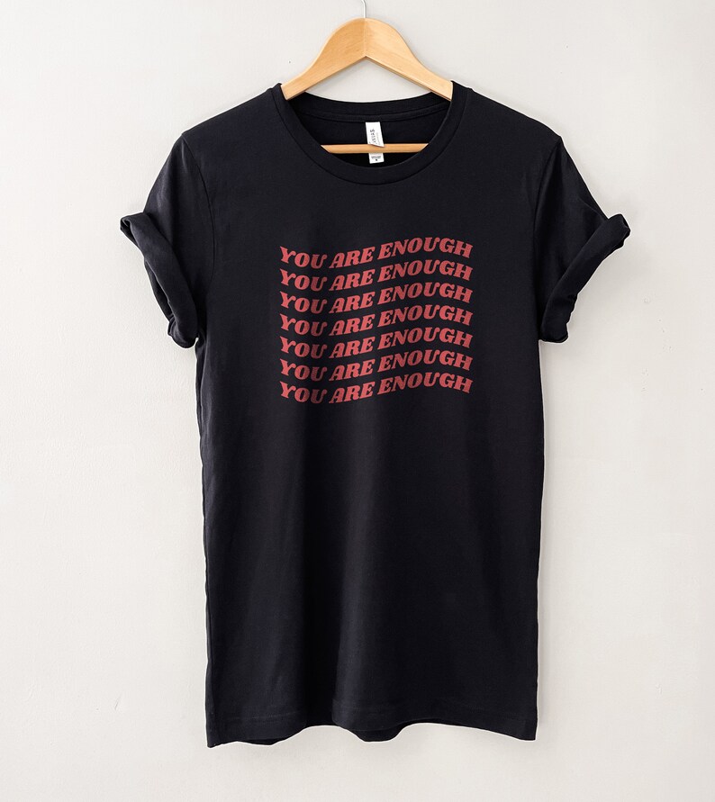 May include: Black t-shirt with the phrase "You are enough" repeated in red lettering.
