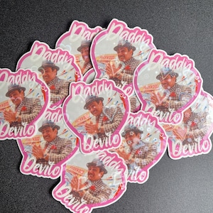 May include: A set of nine pink and white stickers featuring a man in a plaid suit and a hat. The stickers have the text "Daddy Devito" on them.