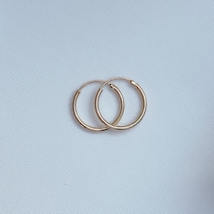 Könnte beinhalten: Ein Paar goldene Creolen. Die Ohrringe sind schlicht und klassisch und eignen sich hervorragend als Geschenk für jeden Anlass.