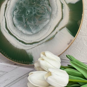 Könnte beinhalten: Ein rundes, grün-weißes Harztablett mit goldfarbenem Rand. Das Tablett hat ein wirbelndes, abstraktes Design. Weiße Tulpen stehen im Vordergrund.