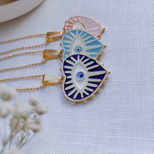 May include: Three gold necklaces with heart-shaped pendants featuring blue evil eyes. The pendants are decorated with white and purple enamel and have a beaded border.