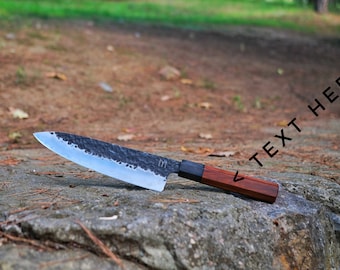 May include: A handcrafted chef's knife with a dark, textured blade and a wooden handle. The blade has a hammered finish and a sharp edge. The handle is a rich, dark brown. The text "TEXT HERE" is visible on the image.