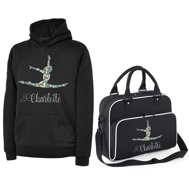 Puede incluir: Sudadera con capucha negra y bolsa de deporte a juego con una silueta de gimnasta plateada brillante y el nombre "Charlotte" impreso en ambas.