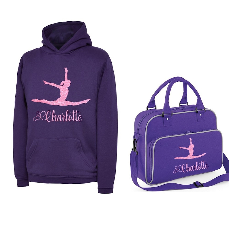 Puede incluir: Sudadera con capucha morada con una silueta de gimnasta rosa y el nombre "Charlotte" en escritura rosa. Una bolsa de deporte morada a juego con el mismo dise&ntilde;o y nombre.