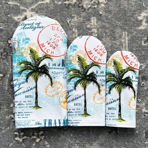 May include: Three white oven mitts with a tropical island theme. The mitts feature palm trees, text that says "Land of Antigua", "Boardwalk Atlantic", and "Registered 19 Miles 50 C.G.O. Barb. Car."