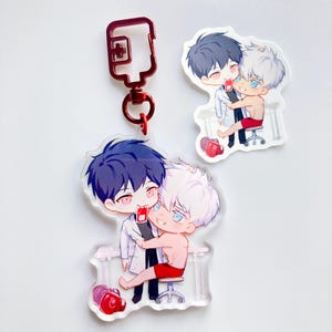 Puede incluir: Un llavero de acrílico transparente con dos personajes de anime. Los personajes son un hombre con cabello negro y un hombre con cabello blanco. El hombre con cabello negro lleva una bata de laboratorio blanca y el hombre con cabello blanco lleva pantalones cortos rojos. El llavero tiene un cierre de metal rojo.