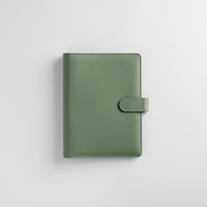 May include: A sage green leather-bound planner with a matching clasp. The cover is smooth and rectangular, with a rounded clasp closure on the right side. The planner is set against a white background.