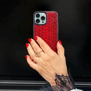 Op de afbeelding: Een smartphonehoesje met een levendig rood, gestructureerd slangenleerpatroon. Het hoesje heeft een zwart frame en een uitsparing voor de camera aan de achterzijde, inclusief drie lenzen en een flitser. Het ontwerp bedekt de achterkant.