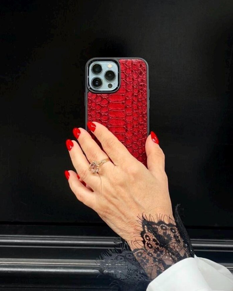 Op de afbeelding: Een smartphonehoesje met een levendig rood, gestructureerd slangenleerpatroon. Het hoesje heeft een zwart frame en een uitsparing voor de camera aan de achterzijde, inclusief drie lenzen en een flitser. Het ontwerp bedekt de achterkant.