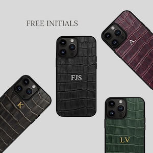 Peut inclure: Quatre coques de smartphone avec un motif texturé en peau de crocodile en noir, rouge foncé, gris foncé et vert foncé. Chaque coque présente une découpe pour triple appareil photo et des initiales personnalisées. Le texte FREE INITIALS est visible.