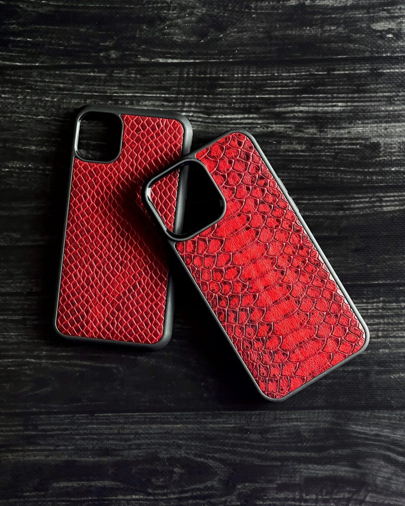 Pode incluir: Duas capas de telefone vermelhas com um padr&atilde;o texturizado de pele de cobra. As capas t&ecirc;m bordas pretas e s&atilde;o exibidas em uma superf&iacute;cie de madeira escura. As capas s&atilde;o projetadas para proteger o telefone.