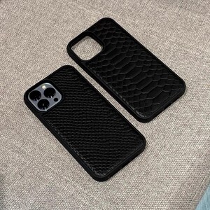 Pode incluir: Duas capas de telefone pretas com superf&iacute;cies texturizadas. Uma capa tem um padr&atilde;o semelhante a escamas e a outra tem uma textura pequena e pontilhada. Ambas as capas t&ecirc;m um recorte para a c&acirc;mera e s&atilde;o projetadas para proteger um smartphone.