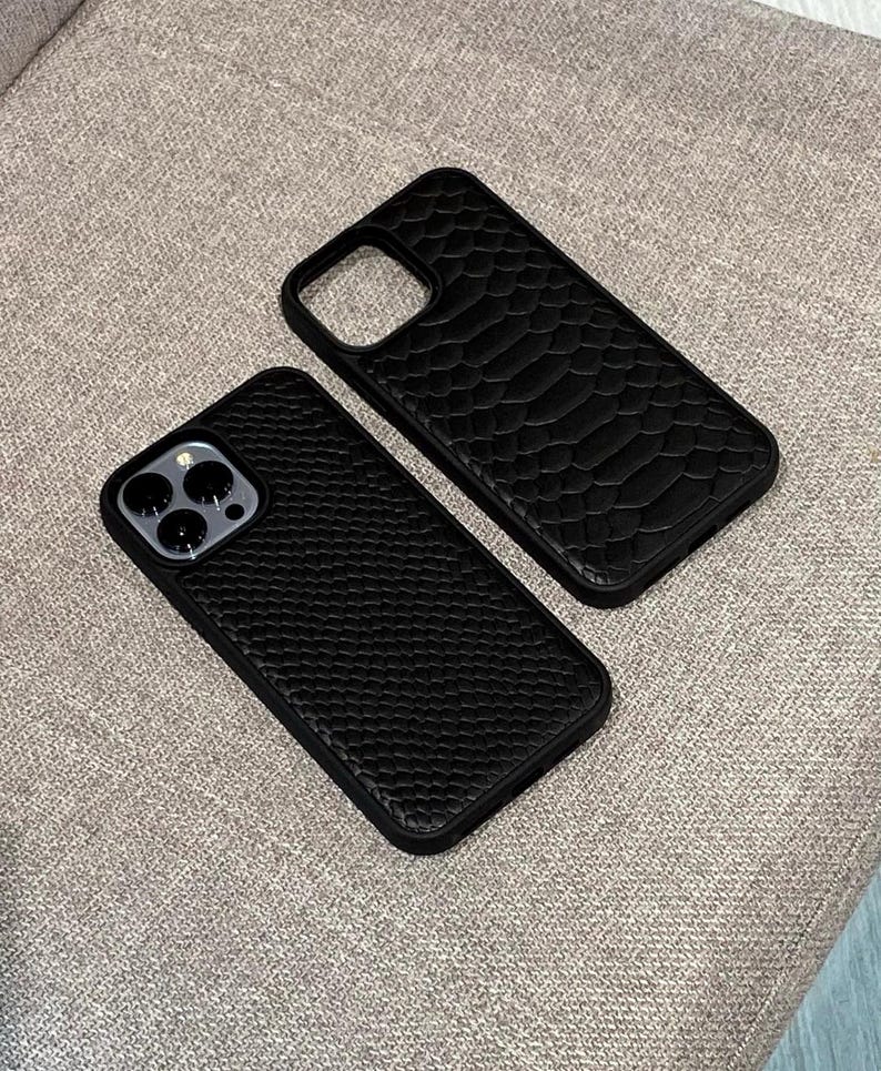 Pode incluir: Duas capas de telefone pretas com superf&iacute;cies texturizadas. Uma capa tem um padr&atilde;o semelhante a escamas e a outra tem uma textura pequena e pontilhada. Ambas as capas t&ecirc;m um recorte para a c&acirc;mera e s&atilde;o projetadas para proteger um smartphone.