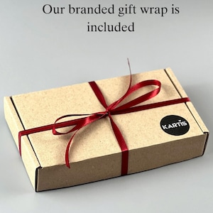 Op de afbeelding: Een rechthoekige kartonnen geschenkdoos vastgebonden met een donkerrood satijnen lint. Een ronde zwarte sticker met de witte tekst KARTIS is op de rechterbovenhoek geplakt. De tekst Our branded gift wrap is included staat boven de doos gedrukt.