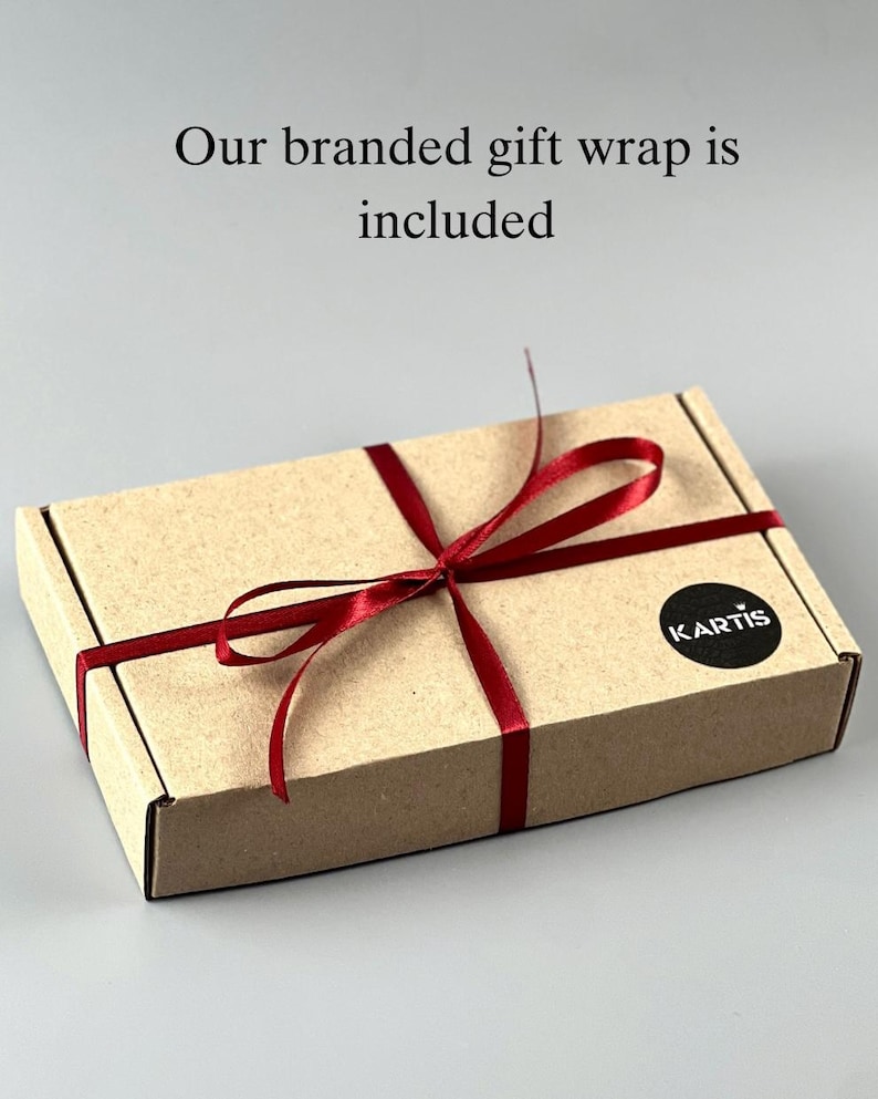 Op de afbeelding: Een rechthoekige kartonnen geschenkdoos vastgebonden met een donkerrood satijnen lint. Een ronde zwarte sticker met de witte tekst KARTIS is op de rechterbovenhoek geplakt. De tekst Our branded gift wrap is included staat boven de doos gedrukt.