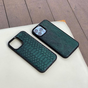 May include: Two green snake-skin textured phone cases with black borders. The cases are lying on a white surface. The phone cases have cutouts for the camera and buttons.