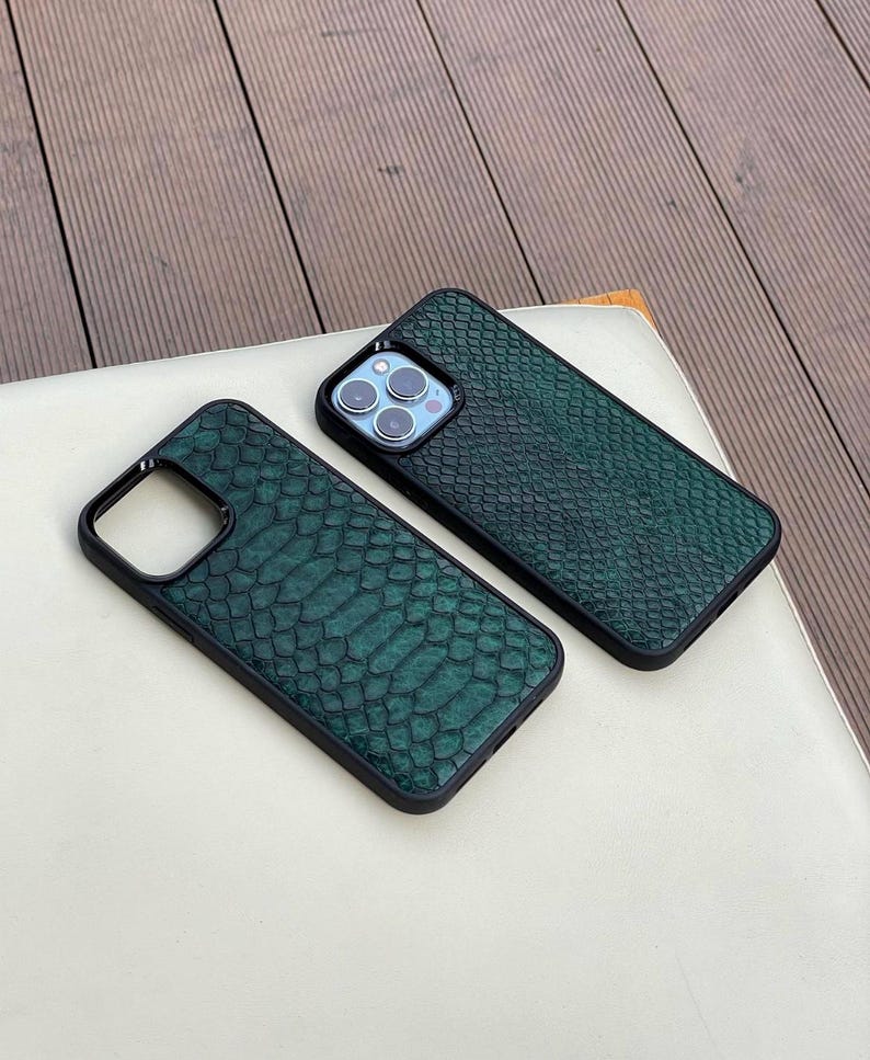 Pode incluir: Duas capas de telefone verdes com textura de pele de cobra e bordas pretas. As capas est&atilde;o sobre uma superf&iacute;cie branca. As capas t&ecirc;m recortes para a c&acirc;mera e bot&otilde;es.
