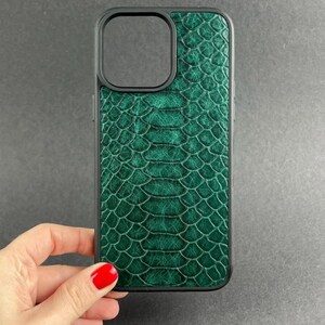 Op de afbeelding: Een donkergroen smartphonehoesje met een gestructureerd slangenleerpatroon. Het hoesje heeft een zwart frame en een vierkante uitsparing in de linkerbovenhoek voor de cameralens, wat zorgt voor een beschermende hoes met schubben.