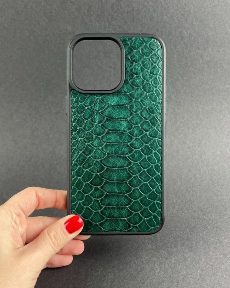 Op de afbeelding: Een donkergroen smartphonehoesje met een gestructureerd slangenleerpatroon. Het hoesje heeft een zwart frame en een vierkante uitsparing in de linkerbovenhoek voor de cameralens, wat zorgt voor een beschermende hoes met schubben.