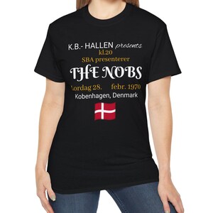 May include: A black short-sleeve t-shirt featuring white and gold text that reads K.B.- HALLEN presents kl.20 SBA presenterer THE NOBS Lordag 28. febr. 1970 Kobenhagen, Denmark, with a small graphic of the red and white Danish national flag below.