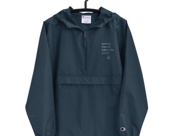 May include: A dark blue Champion brand windbreaker jacket with a zipper closure and a hood. The jacket has a white embroidered message that reads "believe there is light in the world".