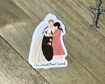 Puede incluir: Una pegatina con una representación de Nuestra Señora del Monte Carmelo, una santa católica, con un velo blanco y un vestido rosa. La pegatina está sobre una superficie de madera.